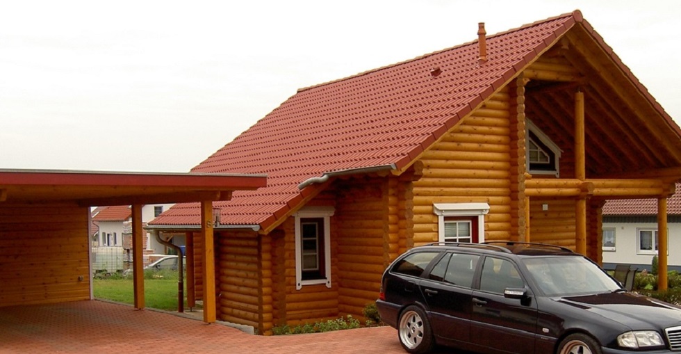 Eine Außenansicht eines attraktiven Blockhauses FINNHOLZ mit mehreren Fenstern und einem hoch aufragenden Dach, umgeben von üppigem Grün.