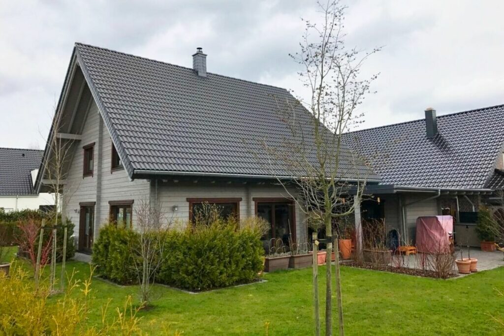 Grau gestrichenes Finnholz Blockhaus mit dunkelgrauer Ziegeldach, umgeben von einem gepflegten Grünbereich.