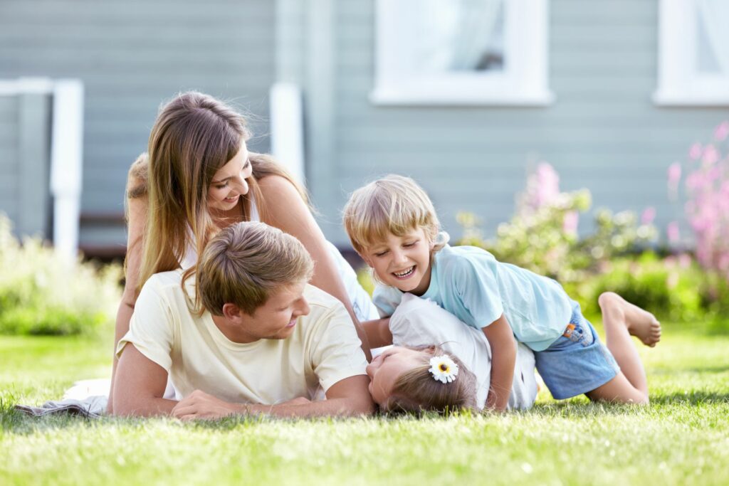 Glückliche Familie mit zwei Kindern, die auf einer Wiese vor einem Blockhaus liegen.