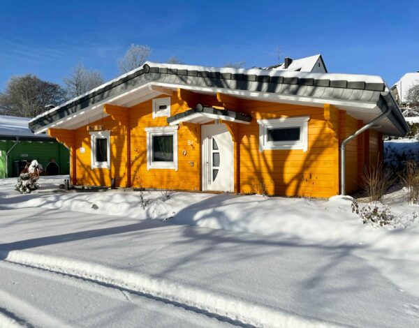 Seitenansicht des schneebedeckten, orangefarbenen Blockhauses von Finnholz.