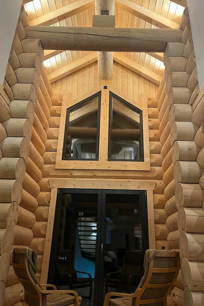 Innenansicht eines Blockhauses mit robusten Holzwänden und modernen Fenstern, die traditionelle und zeitgenössische Elemente vereinen.