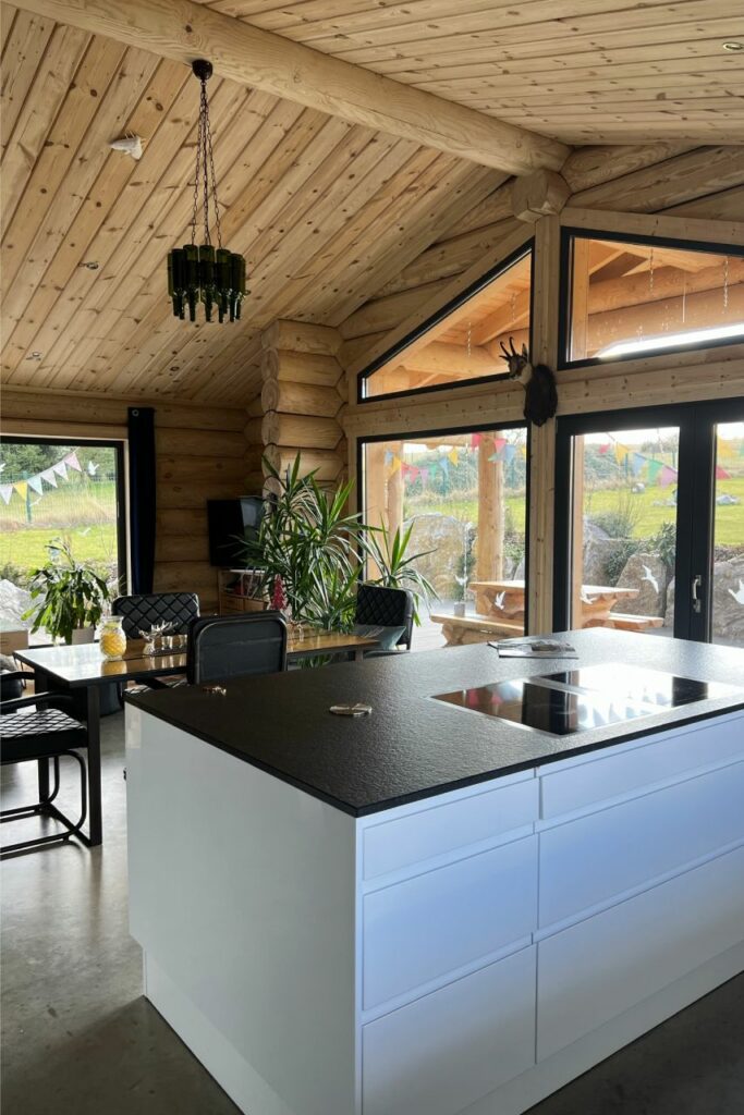 Moderne Küche mit Insel in einem rustikalen Blockhaus mit großen Fenstern und natürlichen Holzelementen.