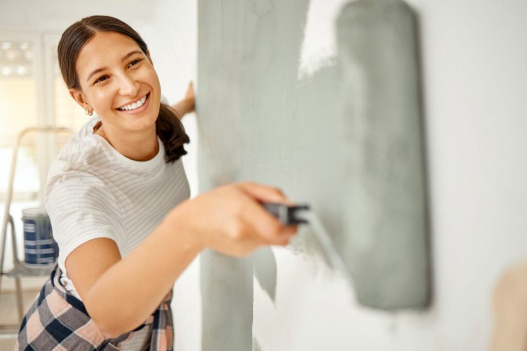 Fröhliche Frau streicht die Wand ihres Hauses selbst.