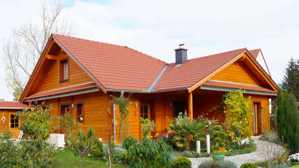 Einladendes FINNHOLZ Blockhaus aus Blockbohlen mit gepflegtem Garten und rotem Dach, repräsentativ für hochwertige Holzhäuser vom Hersteller.