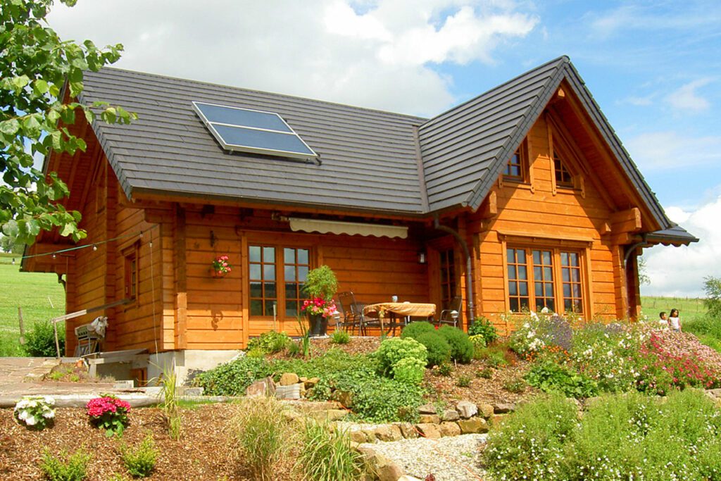 Ökologisches FINNHOLZ Blockhaus mit Solar-Wasserheizung auf dem Dach und einem blühenden Garten.