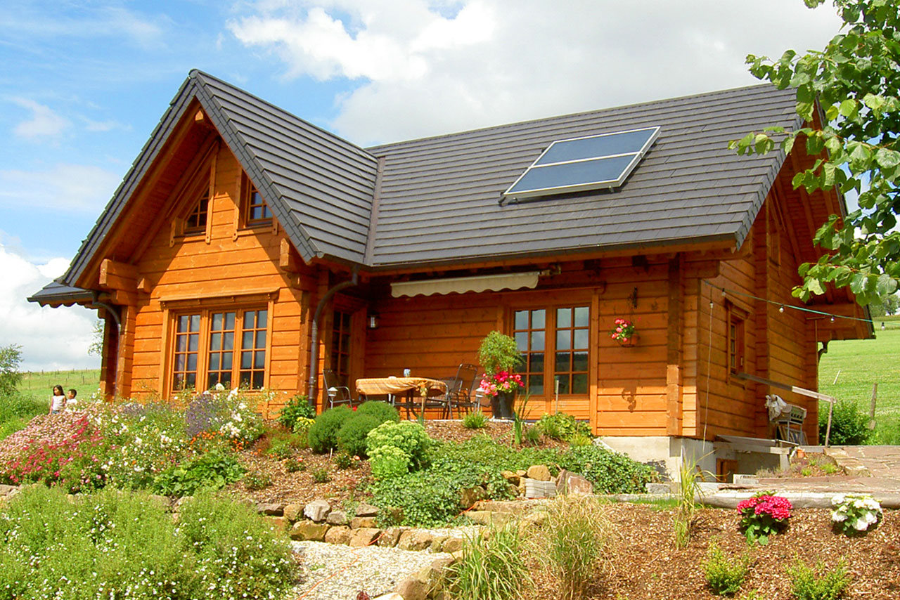 Energieeffizientes Blockbohlenhaus von FINNHOLZ mit Solarpanel und gepflegtem Garten.