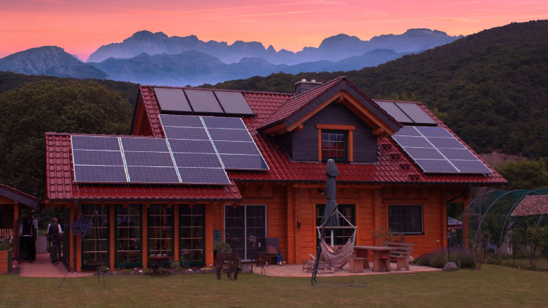 Energieeffizientes FINNHOLZ Blockhaus mit Solarpaneelen vor malerischem Bergpanorama.