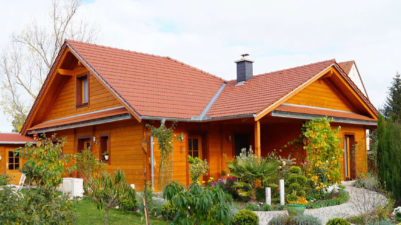 Einladendes FINNHOLZ Blockhaus aus Blockbohlen mit gepflegtem Garten und rotem Dach, repräsentativ für hochwertige Holzhäuser vom Hersteller.